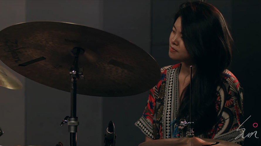 korean female drummer in colorful clothes performing on stage for a live recording with a band