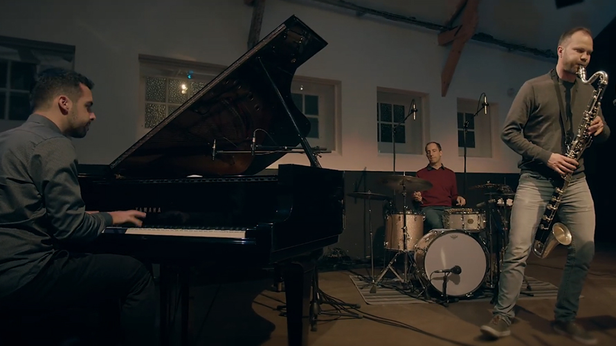 pianist playing a grand piano on stage with a drummer and a clarinet